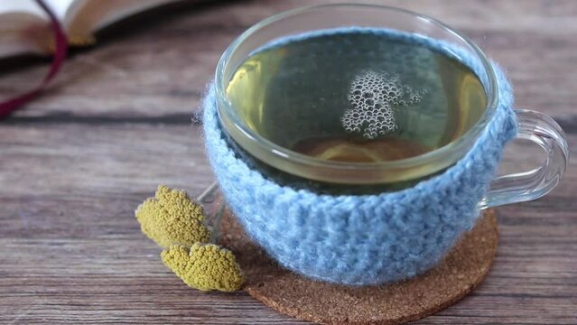 Pouring yarrow (Achillea millefolium) herbal tea in a woolen cup on wood with open holy bible book in the background. Close-up. 