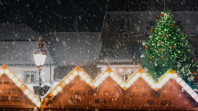 Slowmotion of many snowflakes flying through christmas market and christmas tree. Focus on snowflakes.