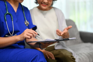 Healthcare worker pointing at clipboard showing health test results to senior patient during home...