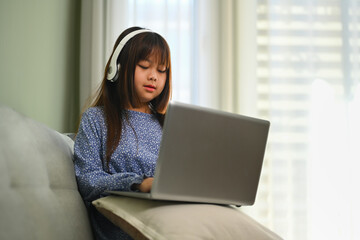 Naklejka premium Cute schoolgirl in headphone watching online virtual class on laptop. Education concept.