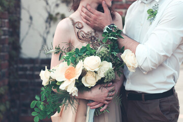 Bride with amazing bouquet of fresh delicate flowers and groom hugging on street