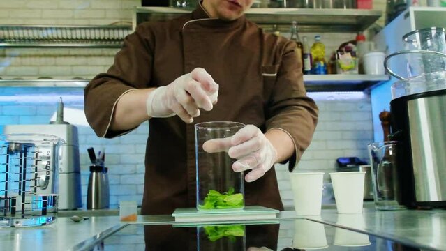 Skilled culinarian cracks chicken egg into transparent measuring cup with spinach. Process of making new gastronomy treasure