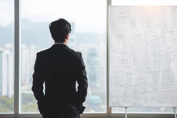 A businessman standing in an office room with a whiteboard. Company business plan strategy idea thinking.