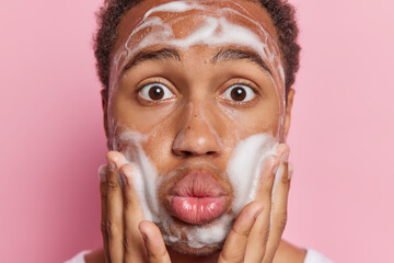 Personal care and hygiene concept. Close up shot of surprised African man washes face with soap...