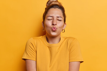 Horizontal shot of cute young woman with hair bun keeps lips folded has eyes closed waits for kiss...