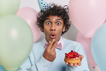 Photo of shocked Hindu man with dark curly hair celebrates special occasion holds small strawberry...