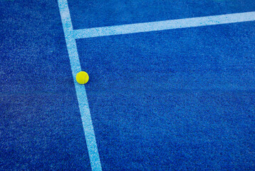 Closeup of one yellow tennis ball with paddle tennis and white lines on blue court. Horizontal...