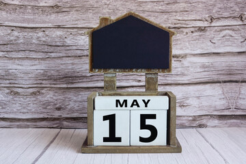 Chalkboard with May 15 date on white cube block on wooden table.