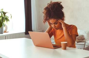 Frustrated African descent young woman in front of laptop at home, receiving e-mail with bad news