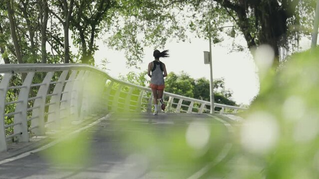rear view of a young asian woman jogger running outdoors in park