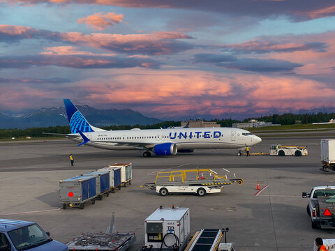 Alaska Airlines Boeing 737 at Ted Stevens Anchorage International Airport in Anchorage, Alaska. Luggage Smiling Inuit face on tail of the Alaska Airlines. Luggage trailers. 