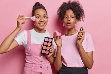 Two women spend time at home together having fun putting make up on hold palette foundation look...