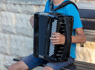 A man plays the accordion while sitting on a bench - obrazy, fototapety, plakaty