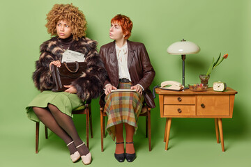 80 lifestyle. Photo of two young fit women sitting on chairs in old room on green background...
