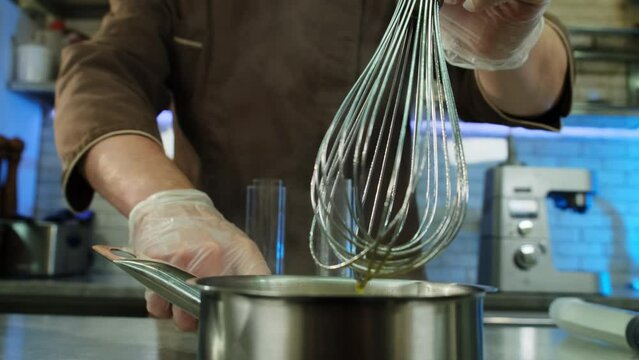 Culinarian turns off stove carefully stirring mixture in saucepan. Combination of ingredients heated to preferred temperature