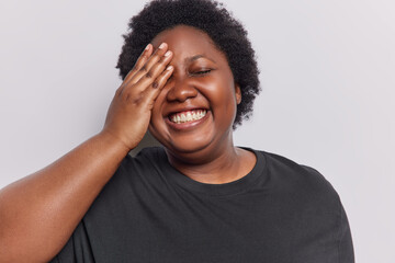 Positive overjoyed chubby African woman laughs gladfully makes face palm smiles broadly expresses...