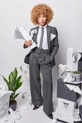 Young african american woman standing in office with desk chair boxes and plants holding papers...