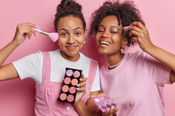 Photo of two young women apply eyeshadow put on makeup want to look beautiful stand closely to each...