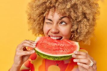 Summer time concept. Curly haired woman holds big slice of juicy watermelon enjoys summer food...