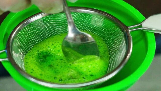 Man stirs egg mixture in sieve with spoon. Professional chef demonstrates proper way to prepare base for dish using funnel