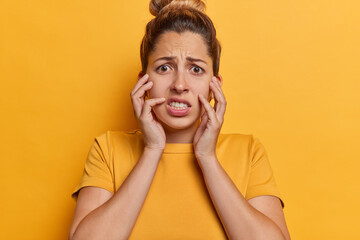 Stressed anxious woman clenches teeth keeps hands on cheeks feels worried and disturbed being...