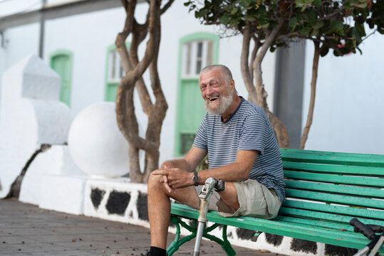 Elderly man with prosthetic leg. left rests sitting on a park bench. Spending a relaxing afternoon. People concept