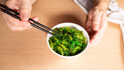 Man holding chopsticks with Japanese seaweed salad over bowl