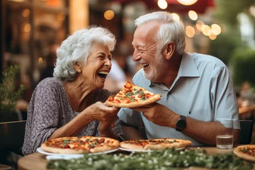 Poster Couple of elderly gentlemen with white hair are smiling while eating a pizza. Celebrating anniversary in pizzeria sitting outdoors. Happy people concept © simona