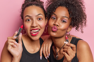 Horizontal shot of two cheerful women apply lipstick with precision enhancing beauty for special...