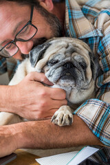 Adult man play with his best friend old dog pug in the office at home - concept of couple people...
