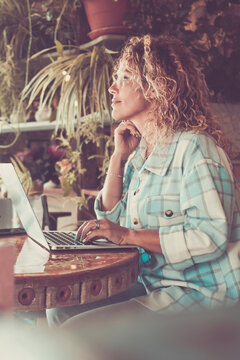 People work at home in smart working job with laptop computer sitting on the table and looking outside the window - happy adult woman smile and enjoy online modern lifestyle