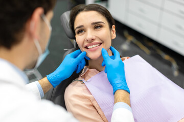 Male dentist checking teeth of an attractive woman, doctor in rubber gloves touches the patient's...