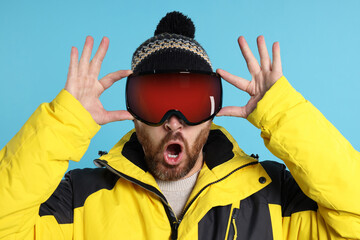 Winter sports. Emotional man in ski suit and goggles on light blue background