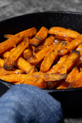 Sweet potato fries cooked in a cast iron frying pan. On a dark stone background