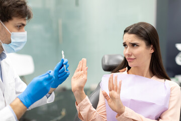 Worried female patient looking at male dentist doctor during check up in clinic, suffering from dental treatment phobia, showing stop gesture with hands
