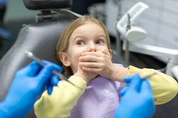 Child girl closing mouth by fear in dental clinic, frightened, afraid of treatment, male doctor in...
