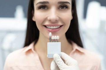 Dentist applying sample from tooth enamel scale to happy young woman patient teeth to pick up right...