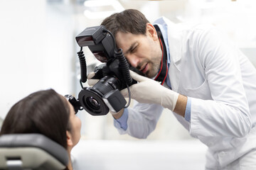Professional male dentist photographing woman teeth with modern digital camera, working in...