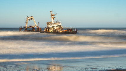 Skeleton Coast, Namibia - August 21, 2022: A long exposure shot captures the blurred motion of the sea around a shipwreck with cormorants perched on its structure.