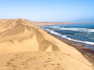 Sandwich Harbour, Namibia - August 22, 2022: A stunning landscape where towering sand dunes seamlessly blend into the crashing waves of the ocean.