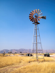 Solitaire, Namibia - August 23, 2022: A rustic windmill stands tall against a vivid blue sky in a golden desert landscape.