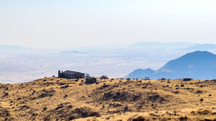 Namib-Naukluft National Park, Namibia - August 24, 2022: A solitary structure stands on a grassy hilltop, overlooking the expansive, flat terrain with distant mountains under a hazy sky