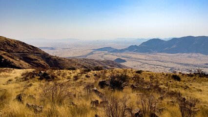 Namib-Naukluft National Park, Namibia - August 24, 2022: Expansive view of a rugged Namibian landscape featuring rolling hills, grassy plains, and distant mountains under a hazy blue sky