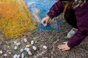 A little diligent lonely girl, a child draws a Ukrainian flag with colored chalk on the asphalt, a...