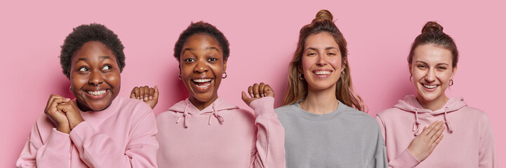 Horizontal shot of four happy women smile broadly express positive emotions react to something nice and funny stand next to each other against pink background. Multiracial female models indoors - obrazy, fototapety, plakaty