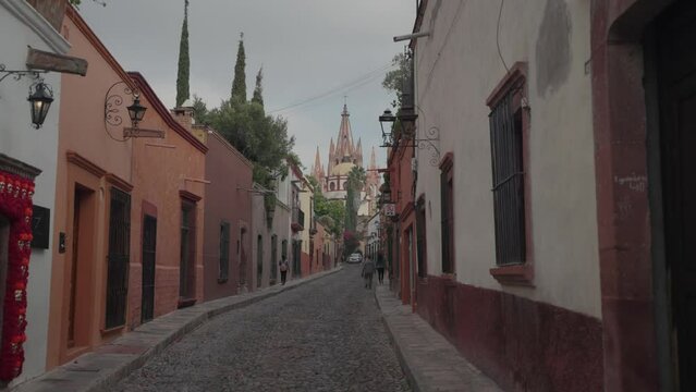 San Miguel de Allende, Mexico - November 9, 2023: Beautiful Hilly Small Narrow Street Alley with Colorful Buildings and La Parroquia de San Miguel Arc&aacute;ngel