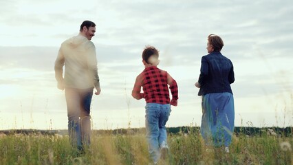 Happy family consisting of parents with little son runs along meadow with plants. Family cherishes...
