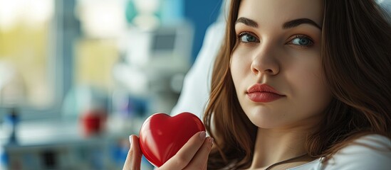 Young woman making blood donation in hospital A woman donates blood while holding a red heart Blood donation. Creative Banner. Copyspace image