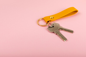 Leather keychain with a key ring on a pink background. Concepts for real estate and moving home or renting property. Buying a property. Mock-up keychain.Copy space.