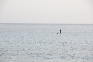 Obraz premium An unrecognizable woman in the distance, paddle surfing completely alone in a calm sea